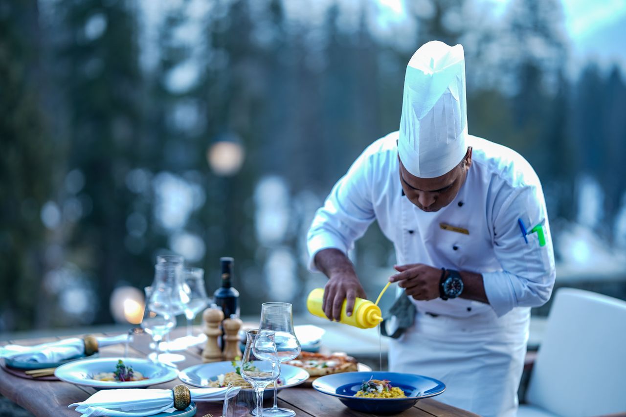 about-us Chef expertly adds finishing touches to a gourmet dish at an outdoor restaurant setting.